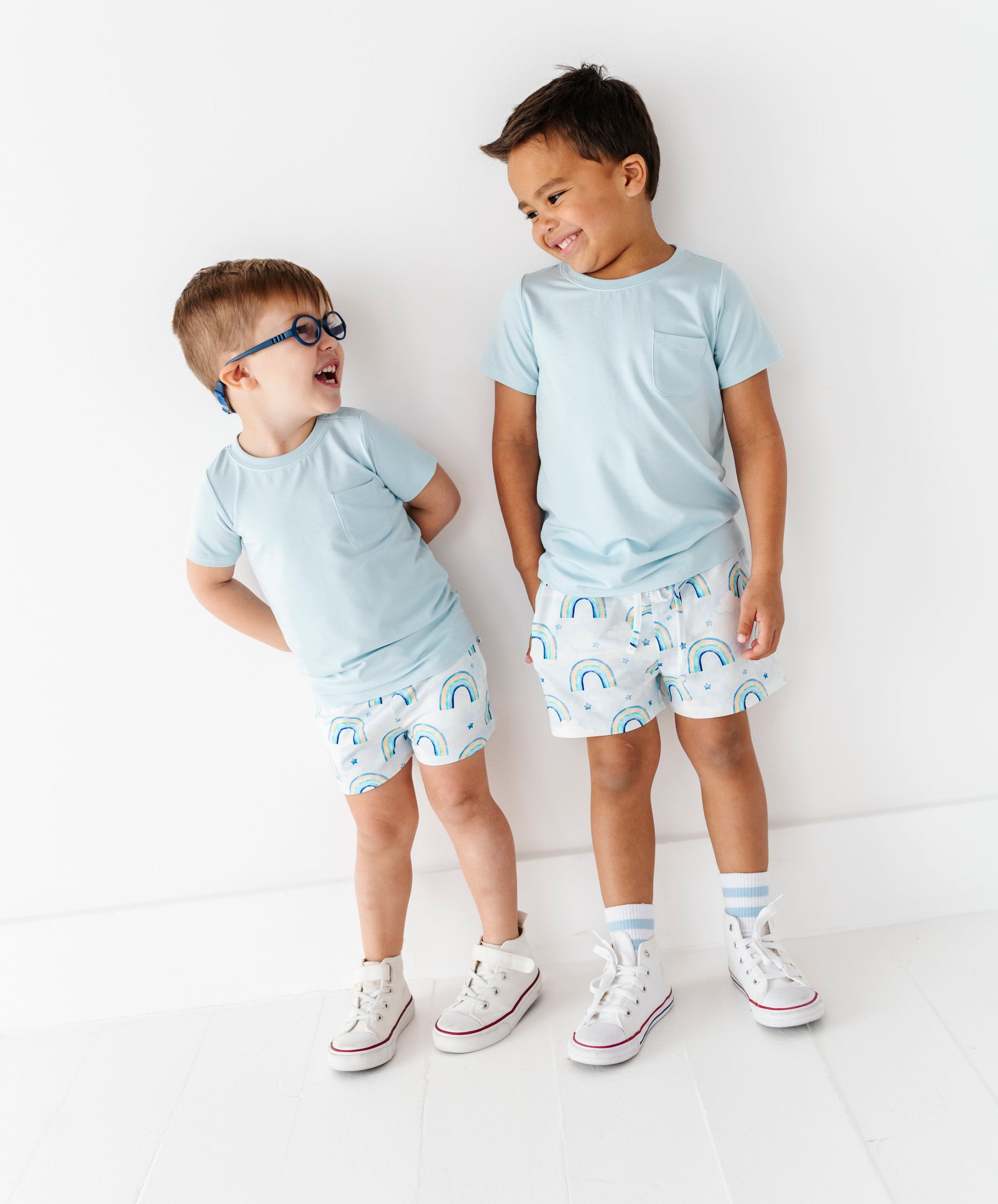 Two children wearing matching light blue shirts and patterned shorts on a white background
