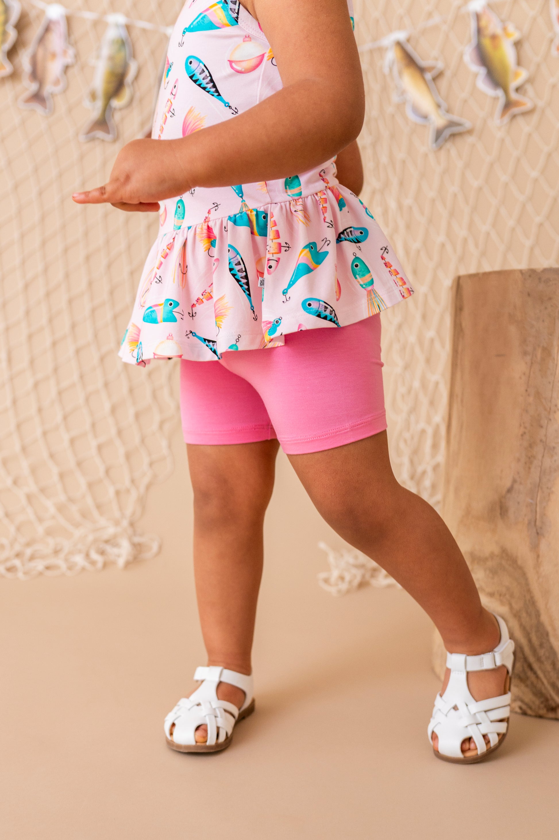 Child wearing a colorful top and pink shorts with a neutral background