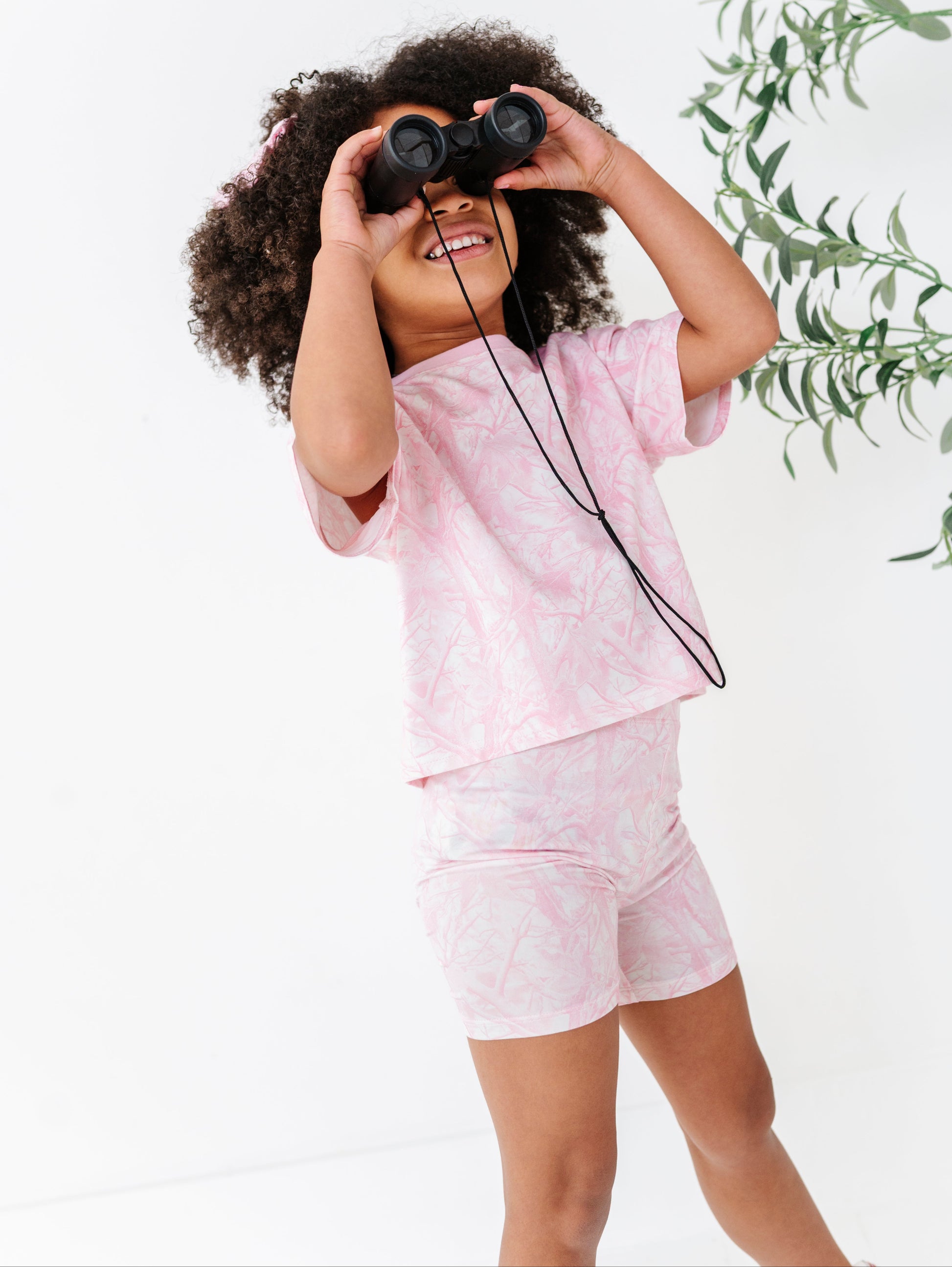 Child in pink outfit with binoculars against a white background