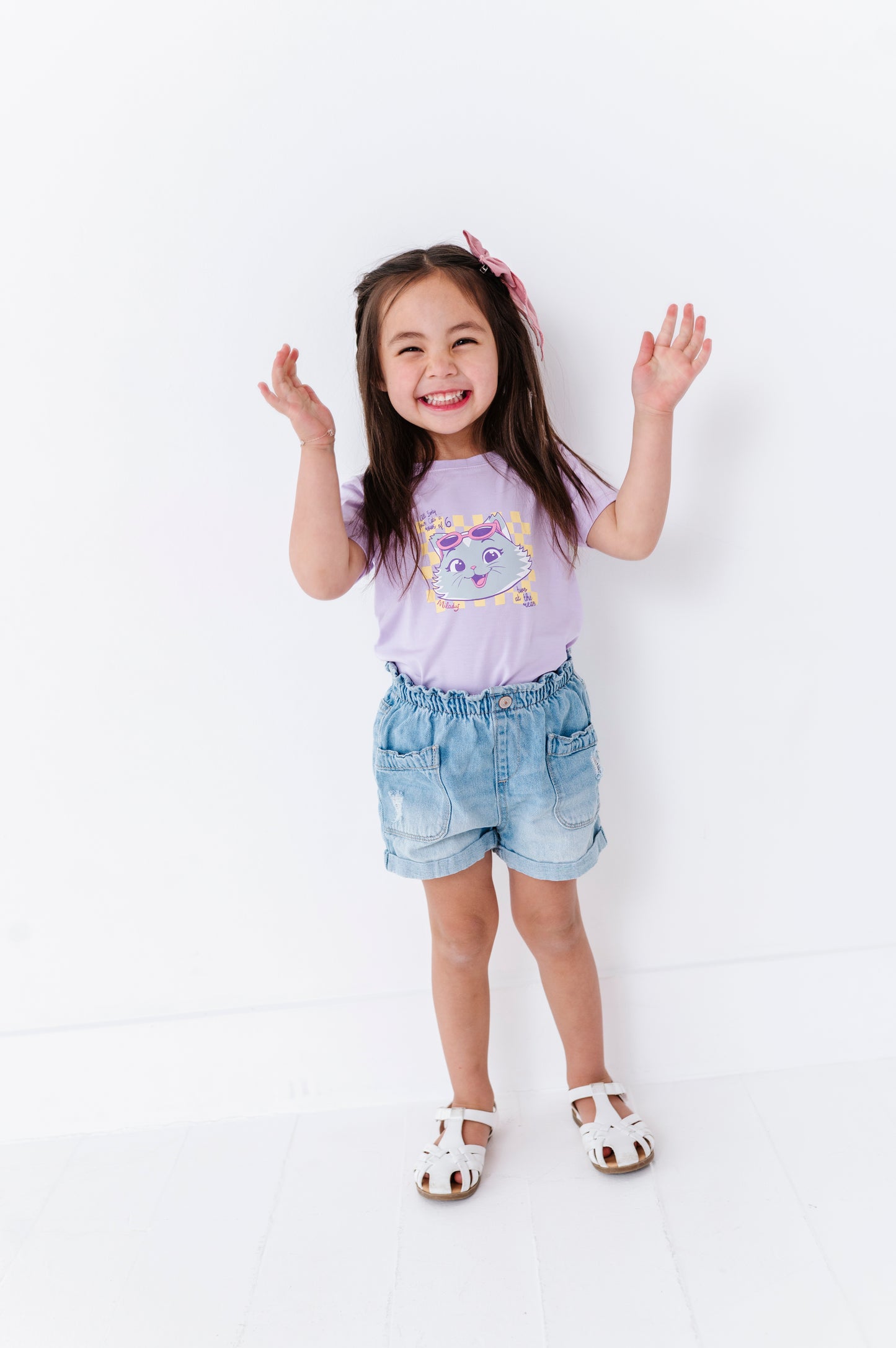 Child wearing a purple t-shirt with a graphic design featuring Milady from 44 Cats and denim shorts on a white background