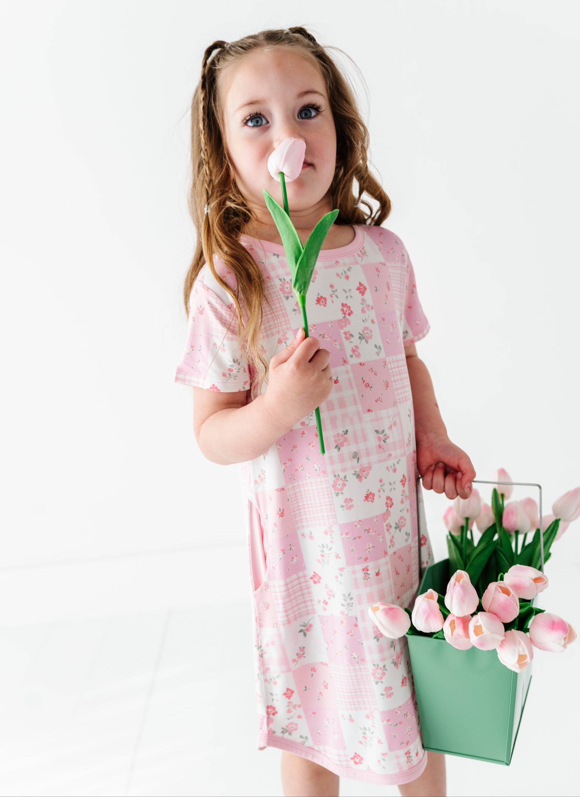 Young girl in a floral bamboo gown holding a tulip and a basket of flowers against a white background