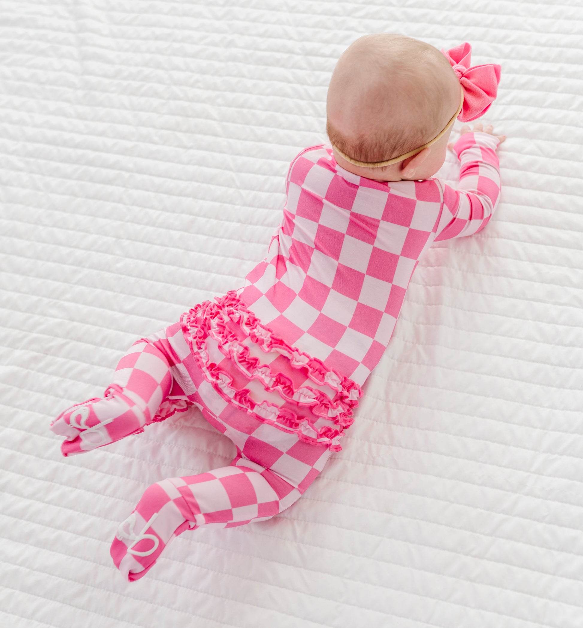 Baby in a pink checkered bamboo outfit lying on a white textured surface