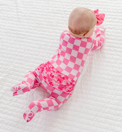 Baby in a pink checkered bamboo outfit lying on a white textured surface