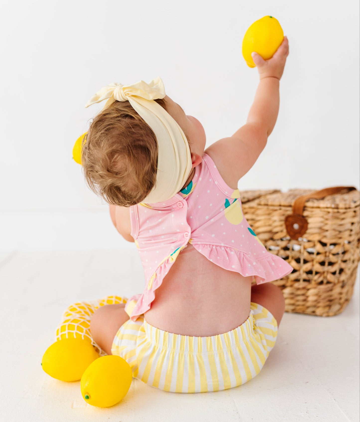 Baby in a pink outfit with lemon-themed accessories on a white background