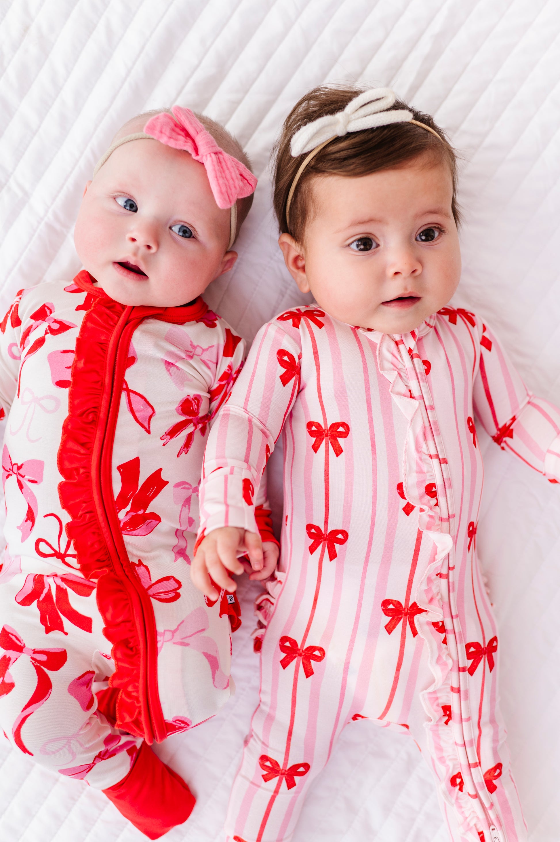 Two babies wearing coordinating Birdie Bean bamboo rompers with ribbon prints