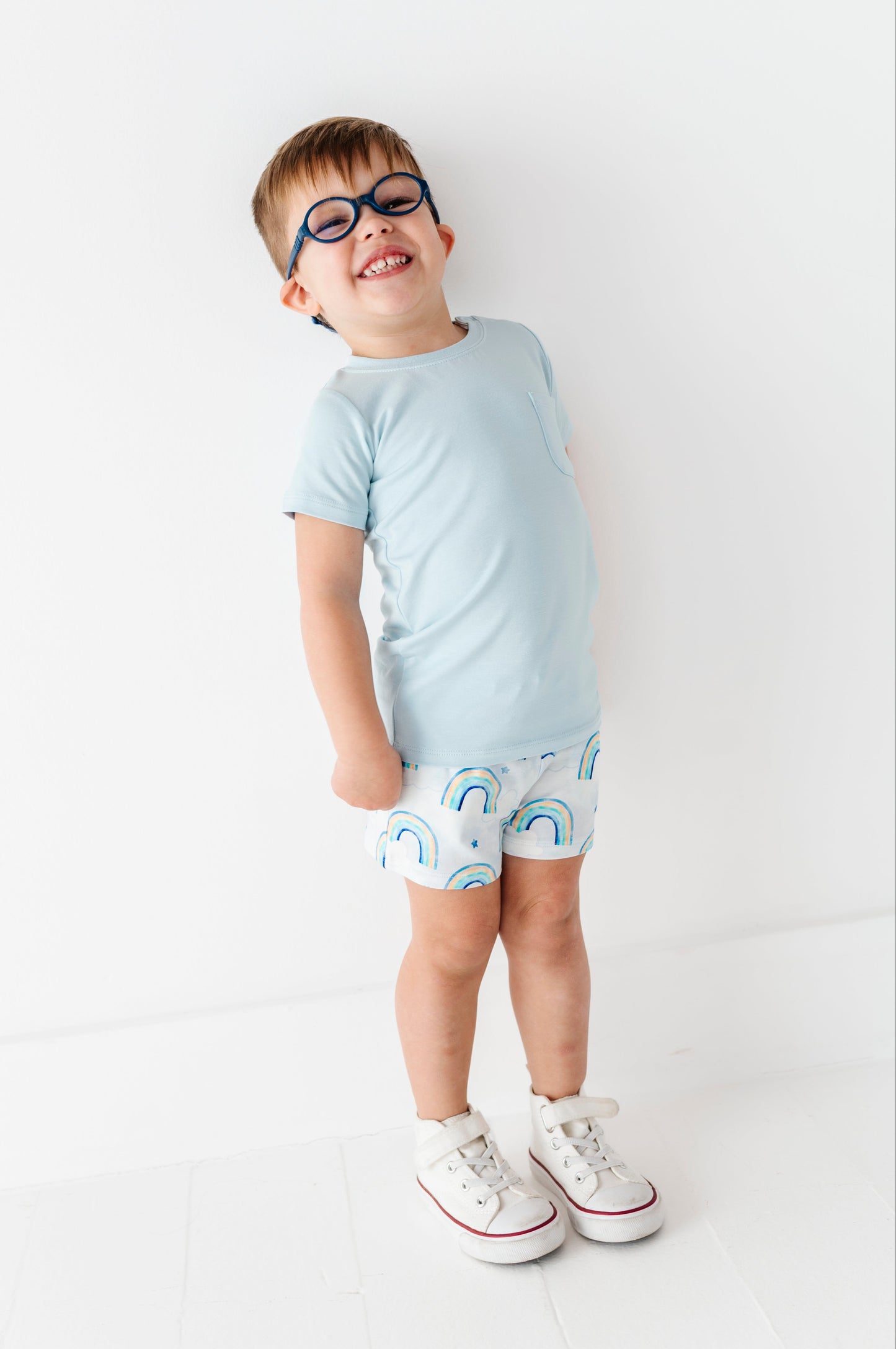 Child wearing a light blue t-shirt and white shorts with rainbow patterns on a white background