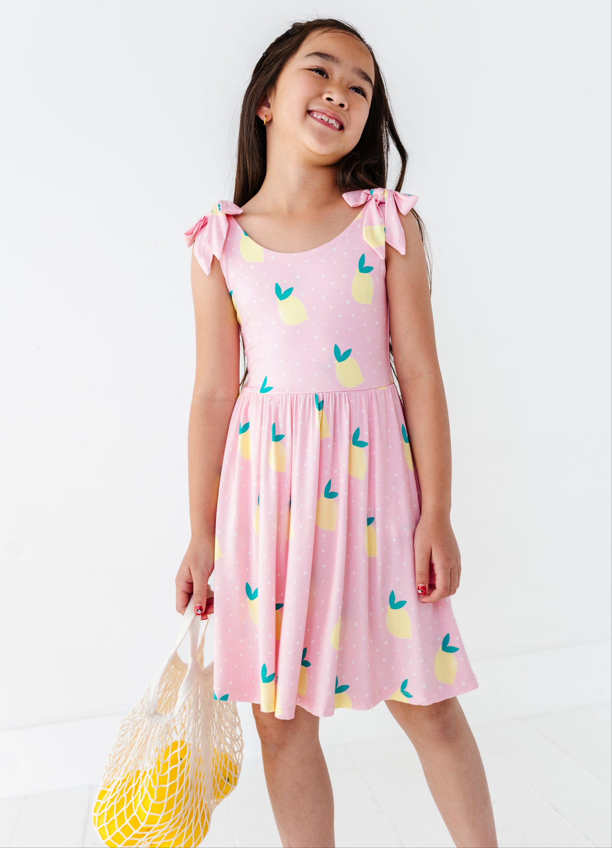 Young girl wearing a pink dress with lemon pattern on a white background