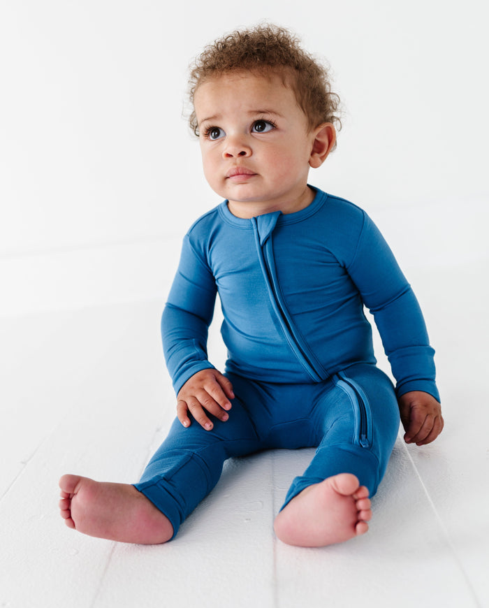 Baby wearing a blue bamboo convertible romper sitting on a white surface