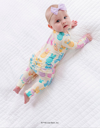 Baby wearing a colorful romper with PEEPS® pattern on a white quilted surface.