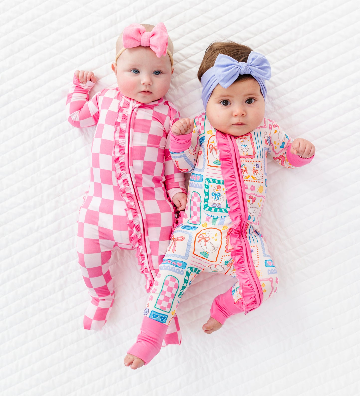 Two babies wearing colorful bamboo rompers and headbands on a white background