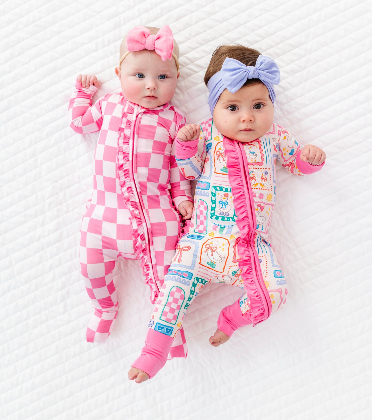 Two babies wearing colorful bamboo zip rompers and headbands on a white background