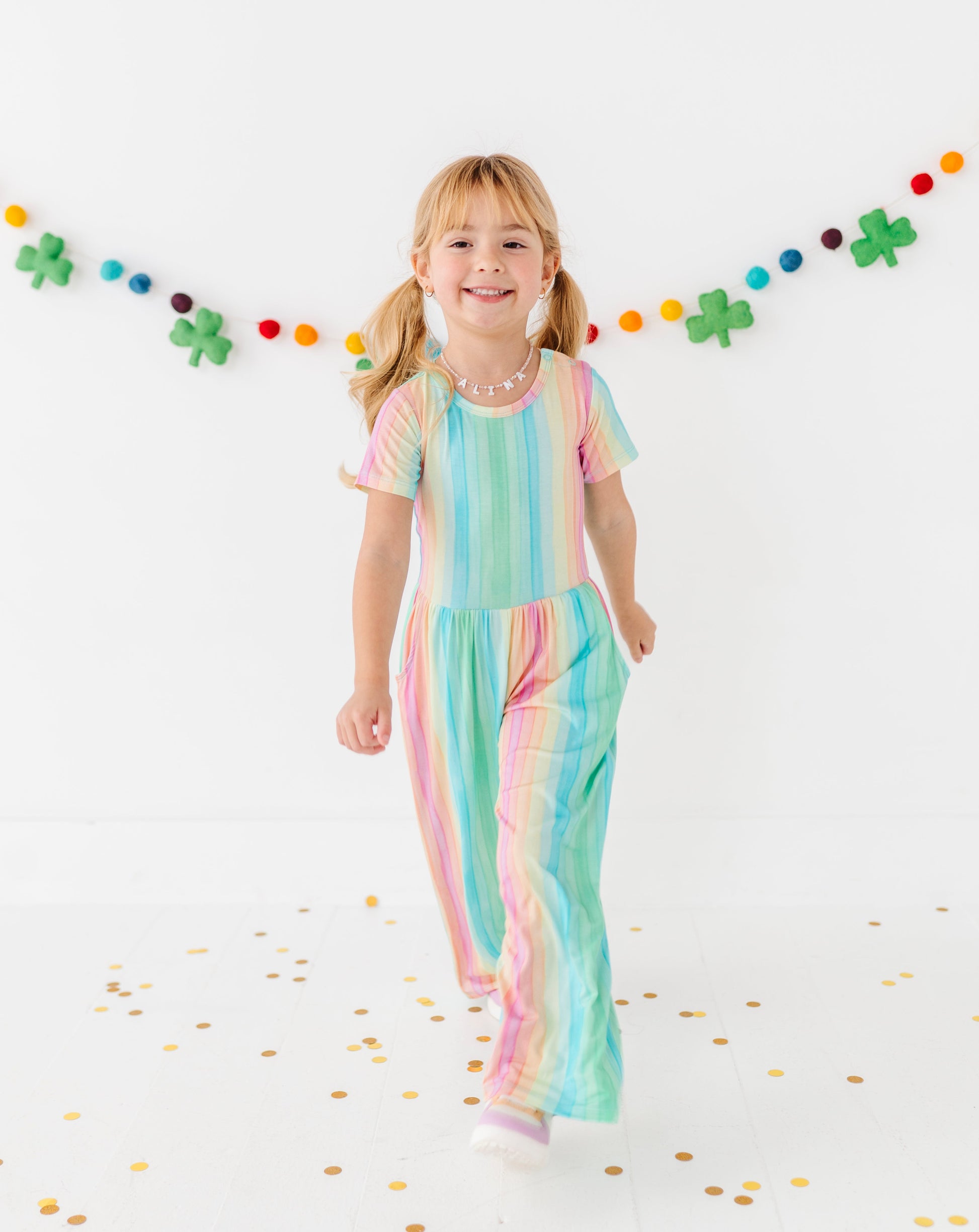 Toddler girl smiling in a rainbow stripe jumpsuit designed for comfort and movement