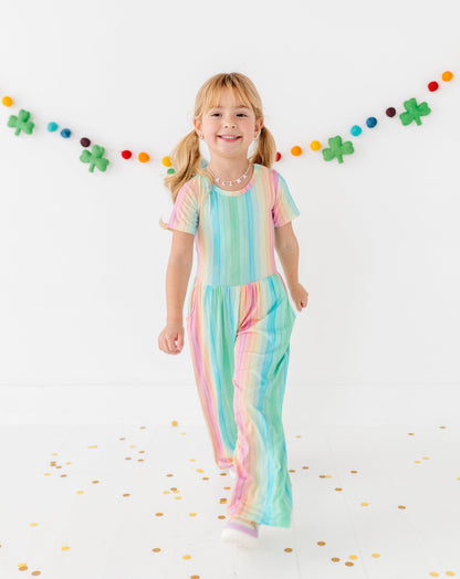 Toddler girl smiling in a rainbow stripe jumpsuit designed for comfort and movement