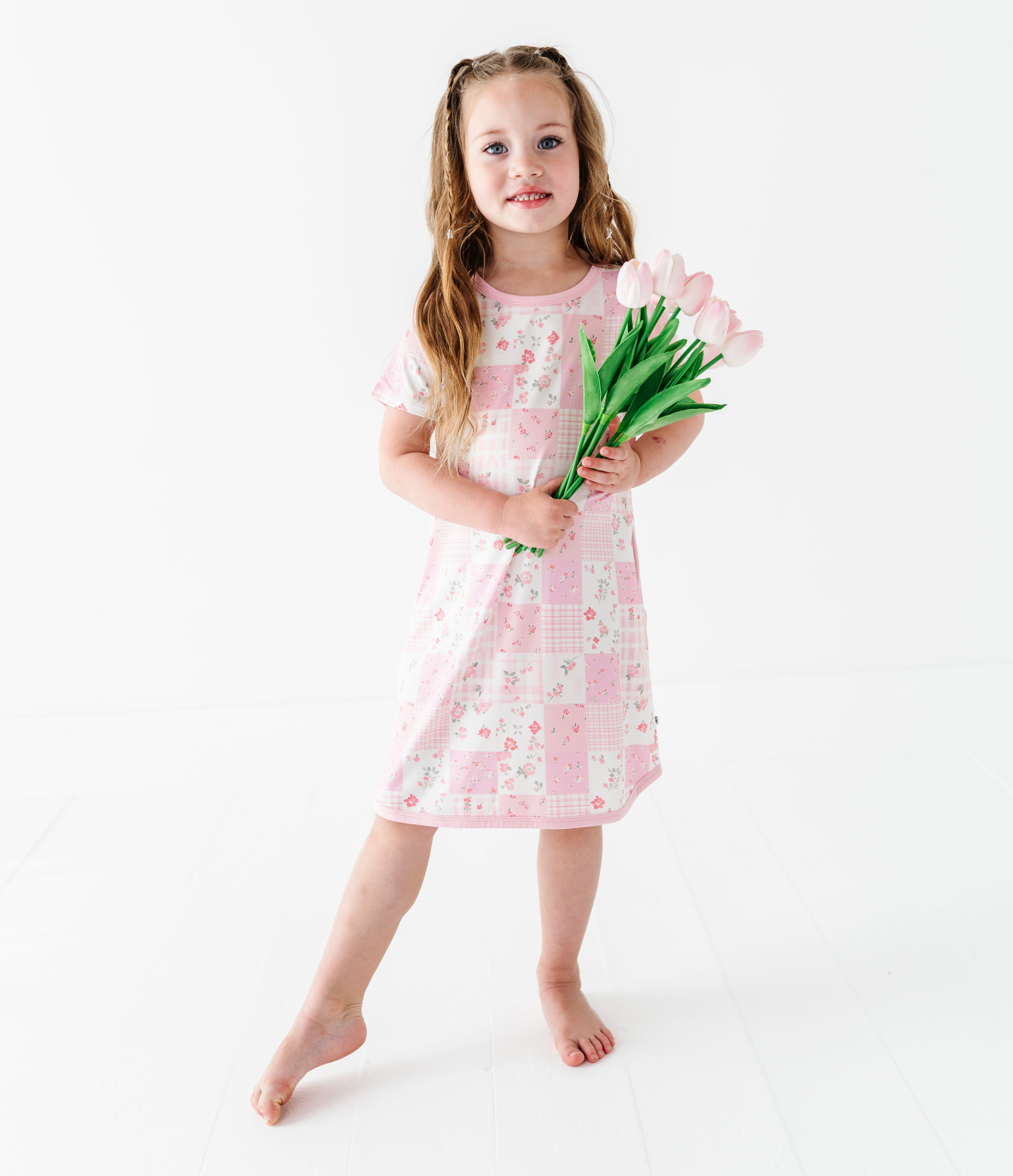 Young girl in a pink floral bamboo gown holding tulips on a white background