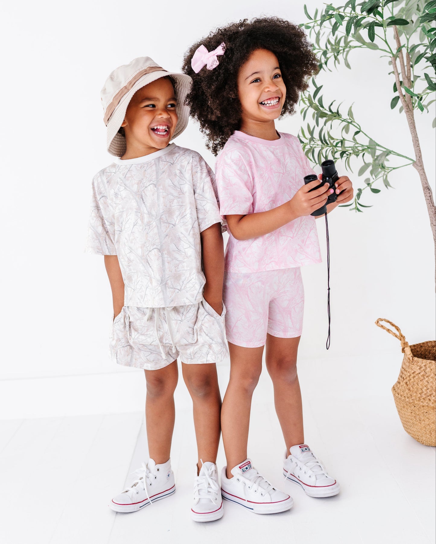Two children in matching outfits standing next to a plant on a white background