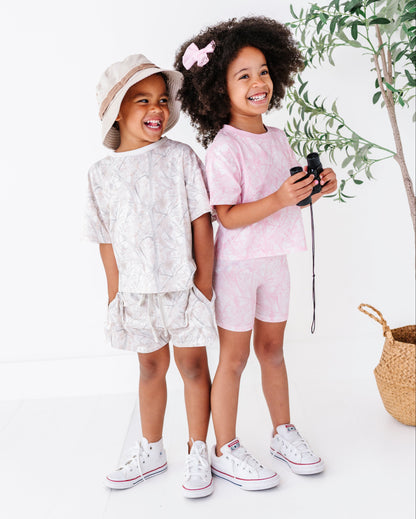 Two children in matching outfits standing next to a plant on a white background
