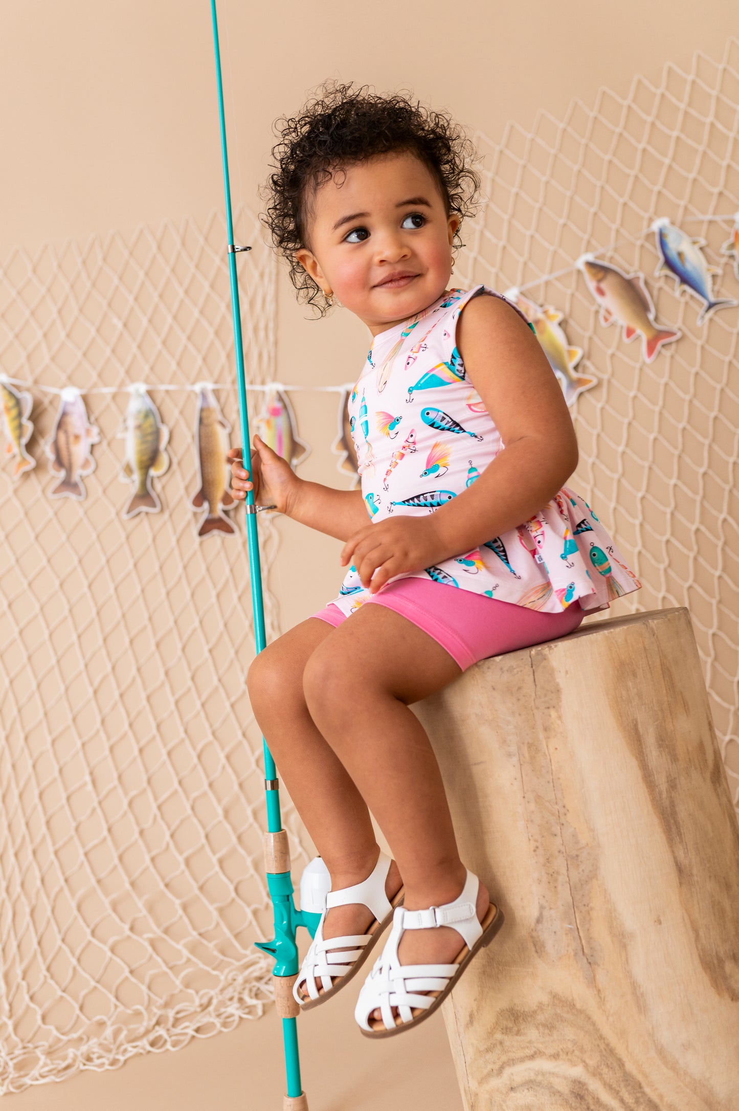 Child sitting on a log holding a fishing rod with a decorative fish banner in the background.