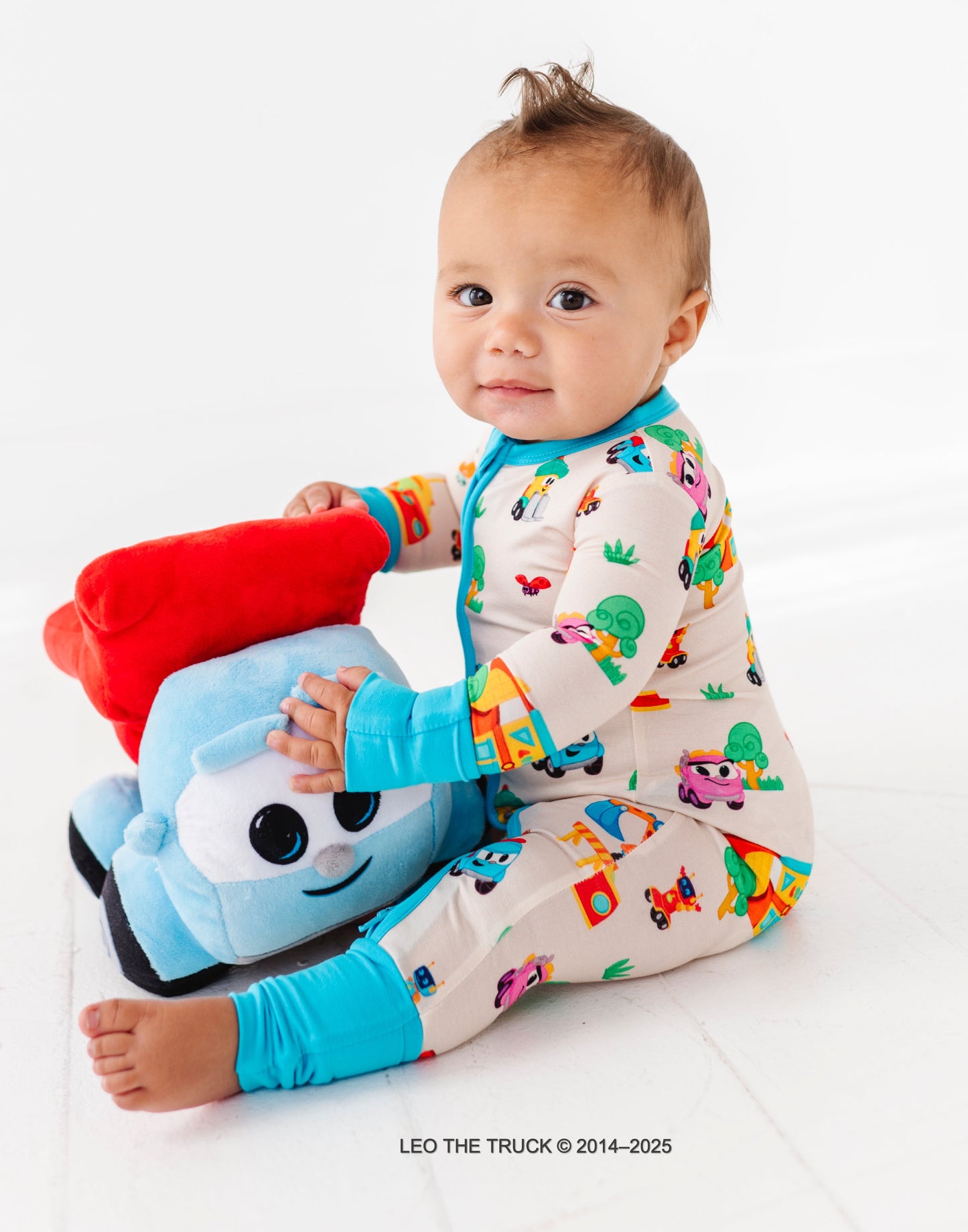 Little boy playing with Leo the Truck plush toy while wearing bamboo Leo the Truck convertible romper 