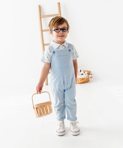 Child wearing light blue overalls and holding a basket on a white background