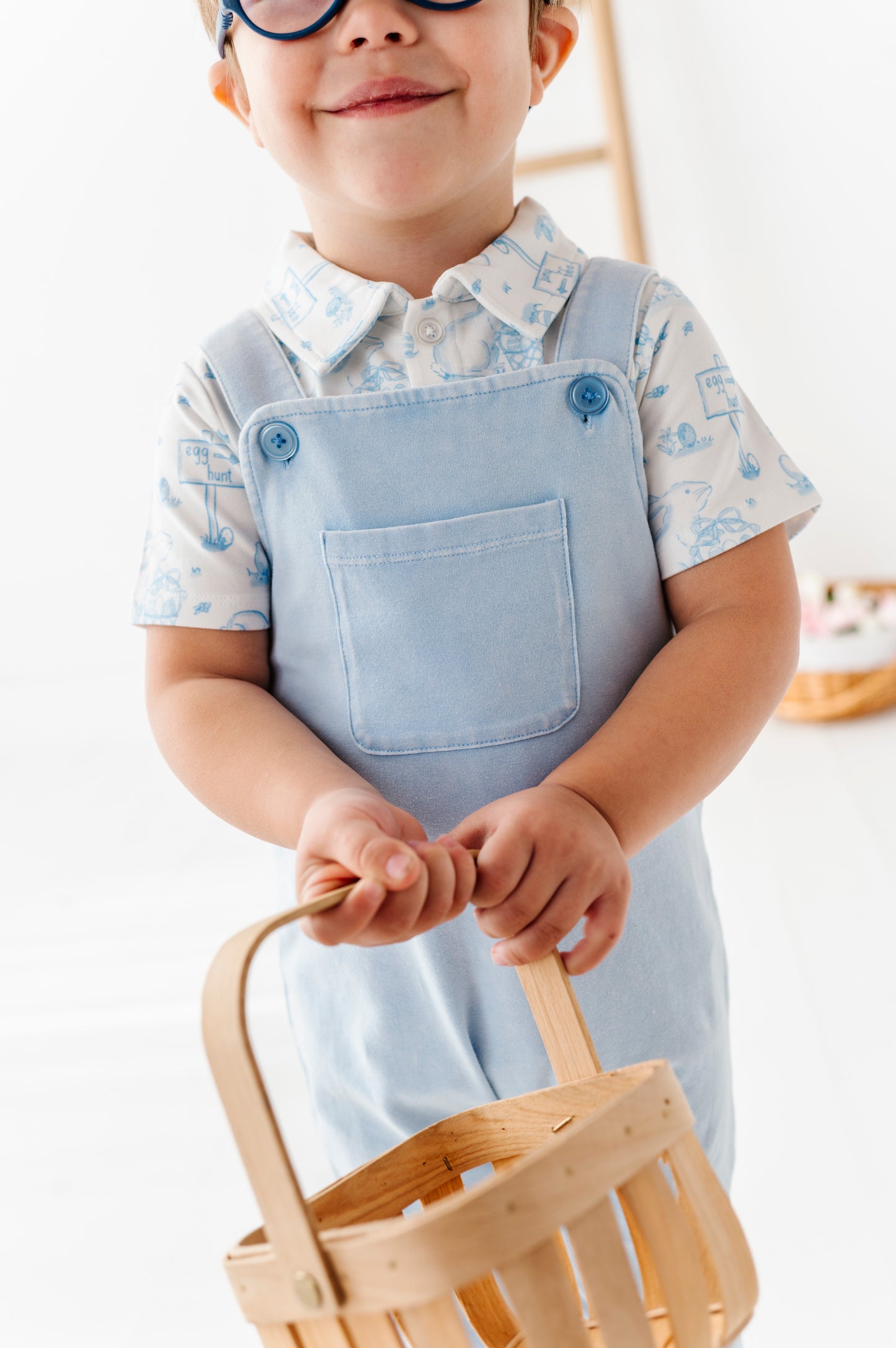Child wearing a light blue dress over a patterned shirt, holding a wooden basket.