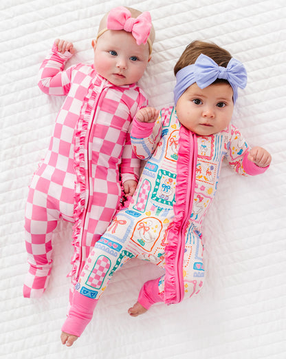 Two babies wearing pink and checkered bamboo pajamas with headbands on a white background