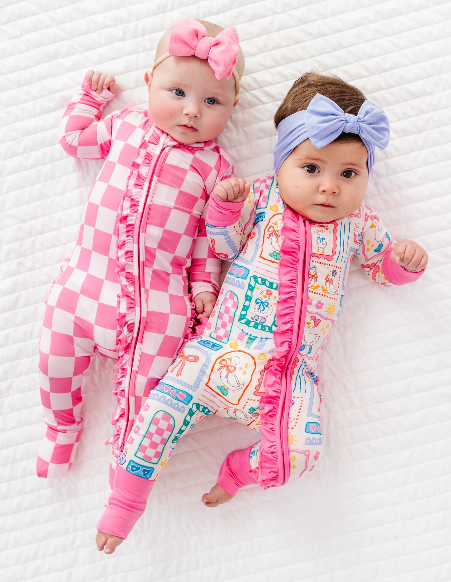 Two babies wearing pink and checkered bamboo rompers with headbands on a white background
