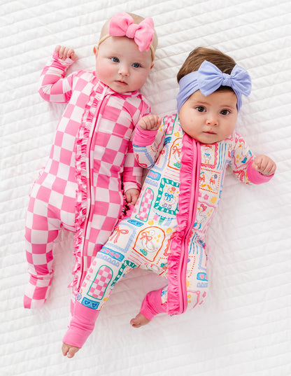 Two babies wearing pink and checkered bamboo rompers with headbands on a white background