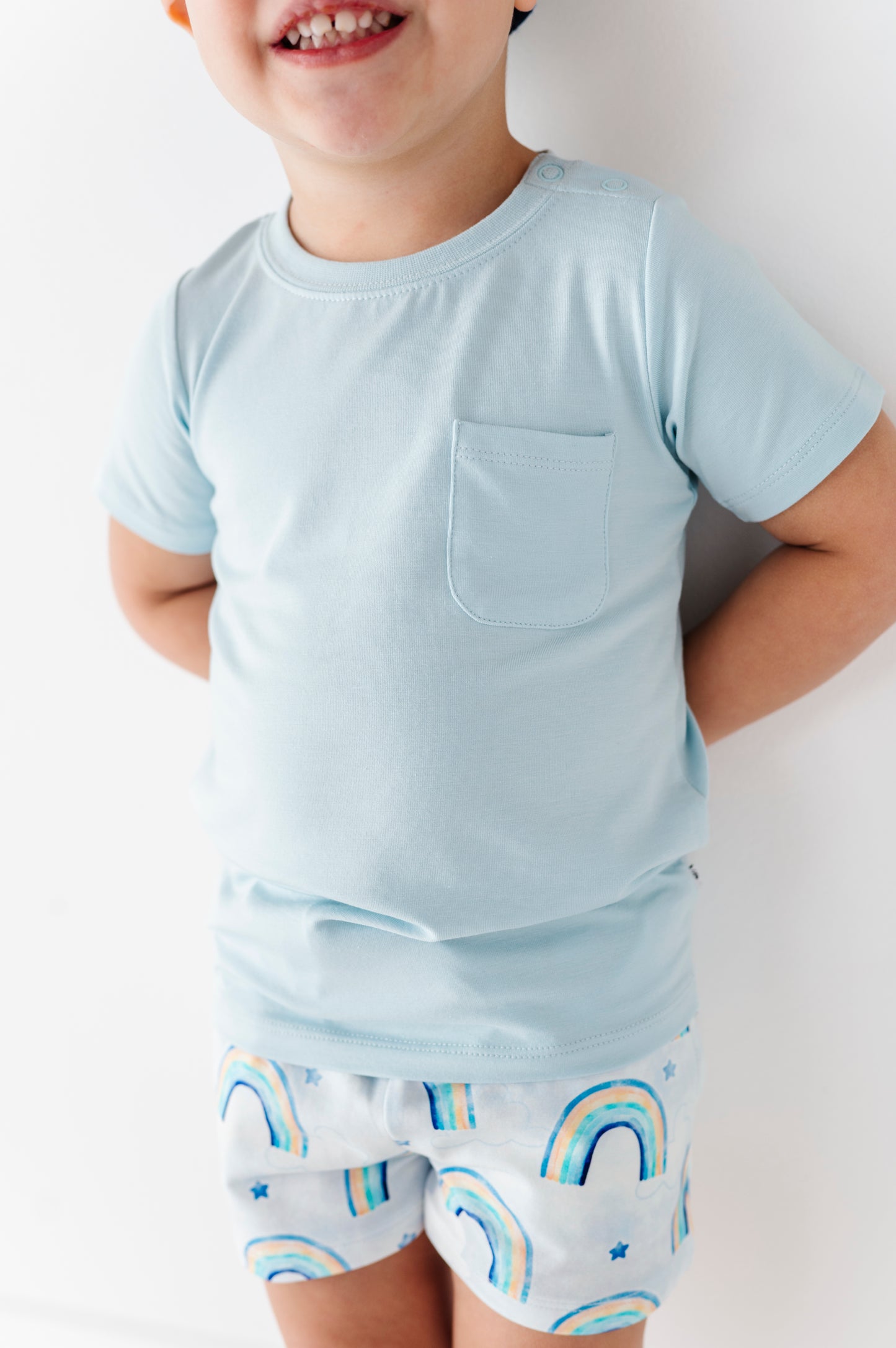 Child wearing a light blue bamboo shirt and matching bamboo cotton shorts with rainbow patterns on a plain background