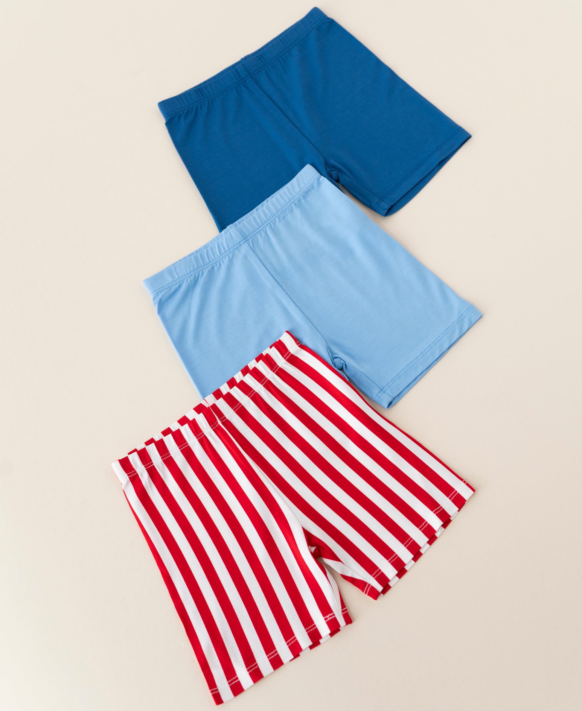 Three pairs of bamboo biker shorts in blue, red and white stripes, and cobalt blue on a beige background
