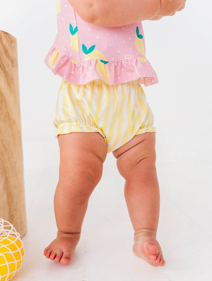 Child wearing a pink top and yellow striped shorts on a white background
