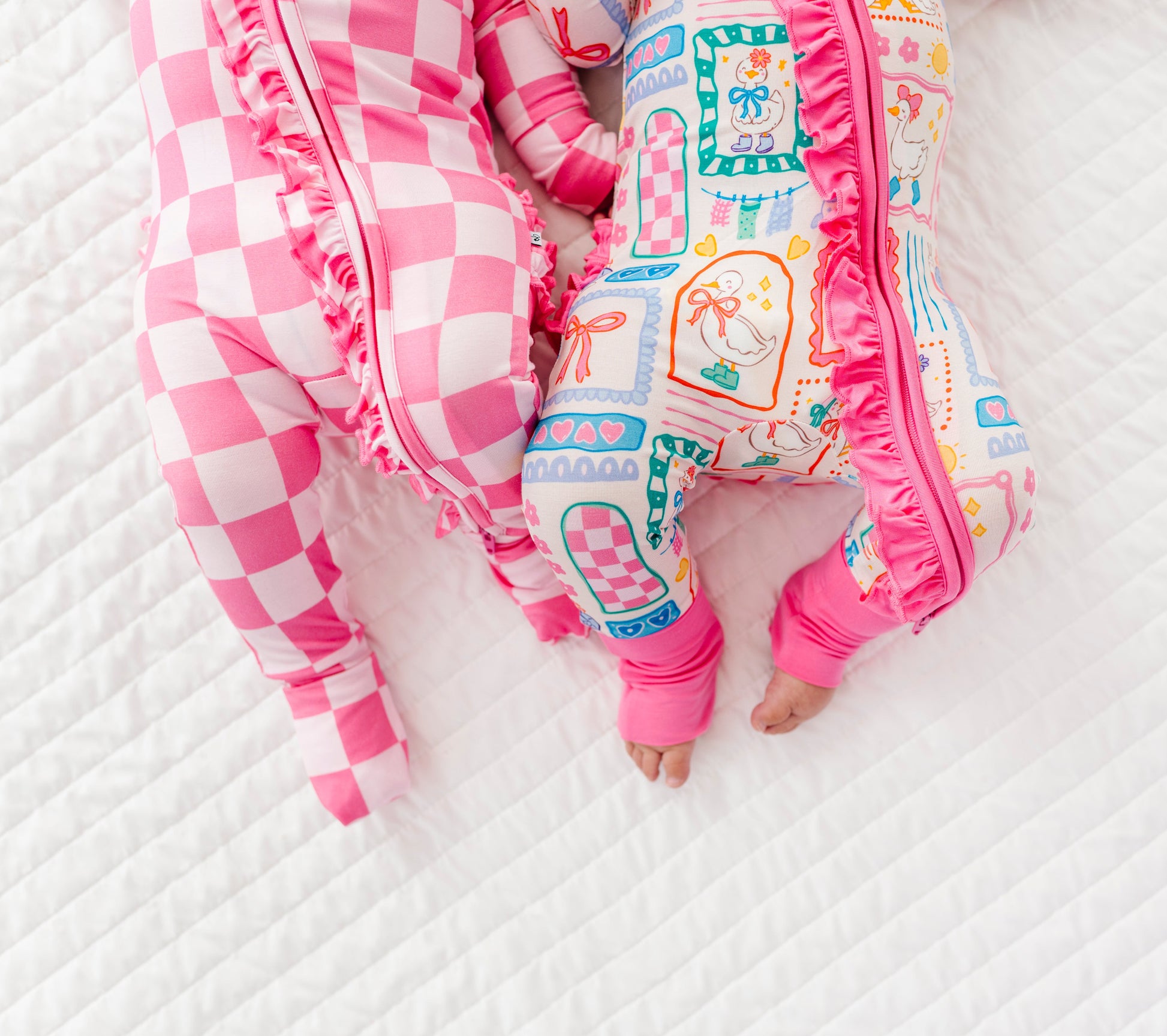 Two babies in colorful bamboo zip rompers lying on a white textured surface