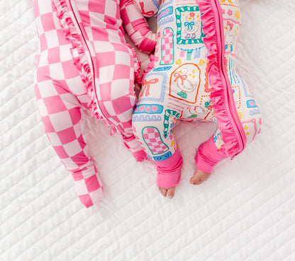 Two babies in colorful bamboo zip rompers lying on a white textured surface