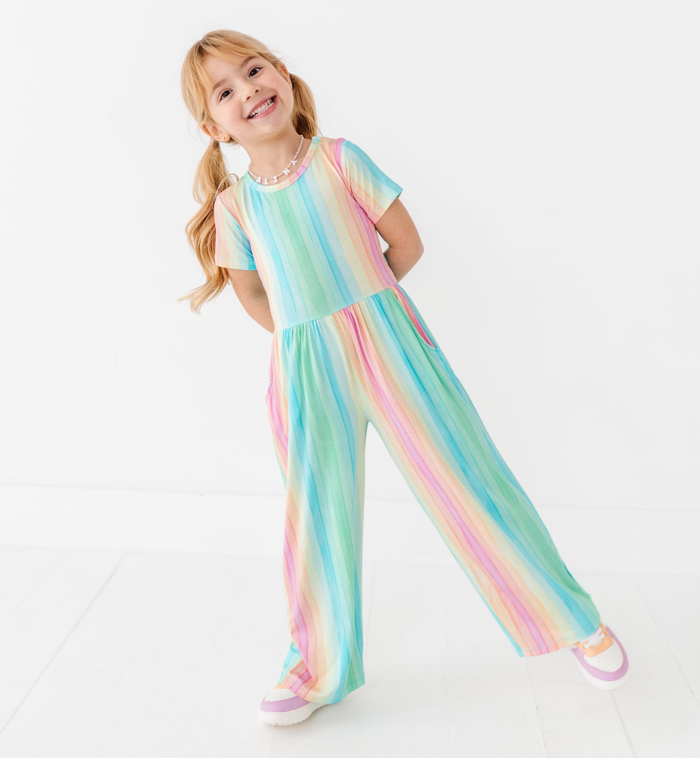 Toddler girl wearing a rainbow stripe bamboo jumpsuit with short sleeves and wide legs
