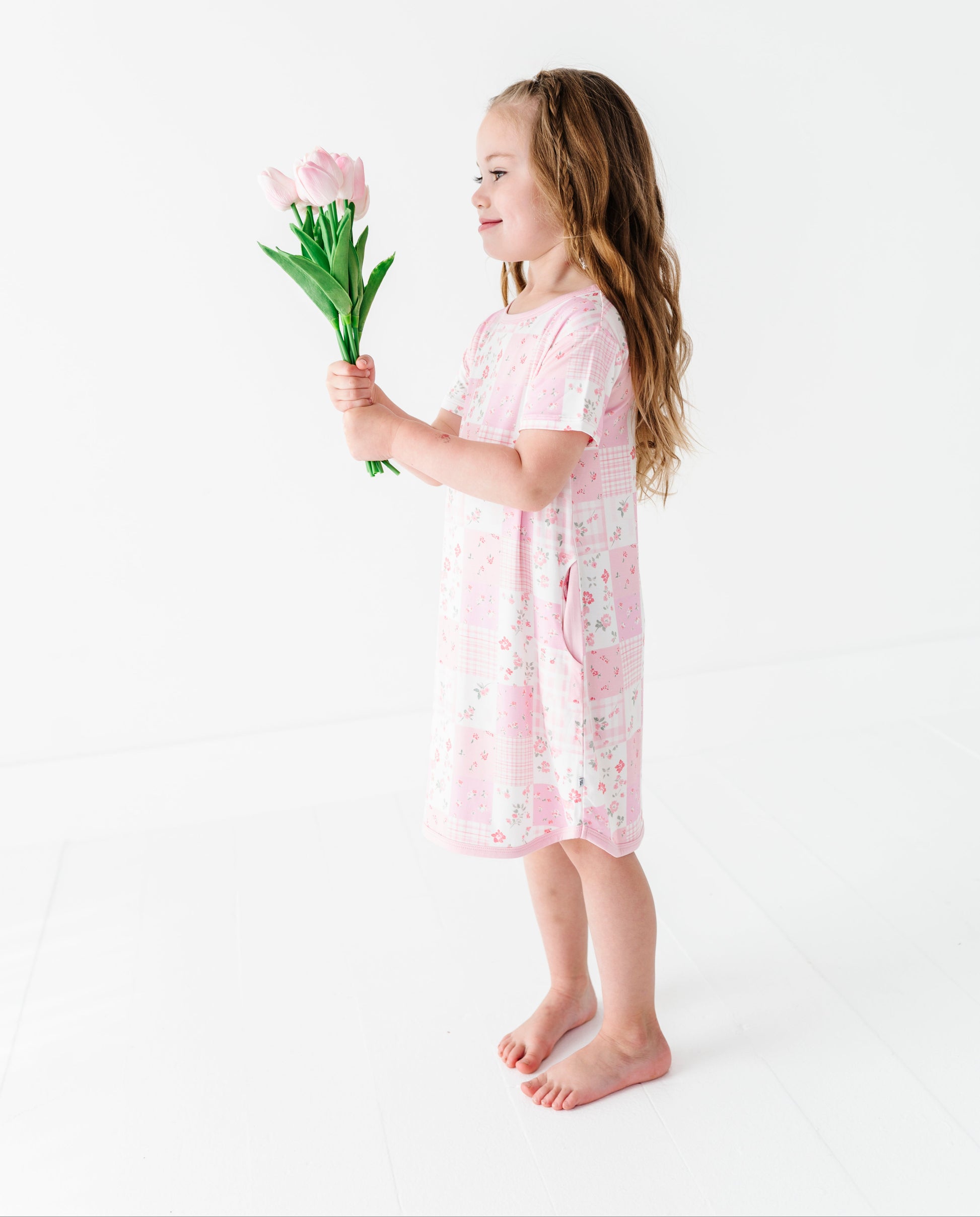Young girl in a pink bamboo nightgown holding a tulip against a white background