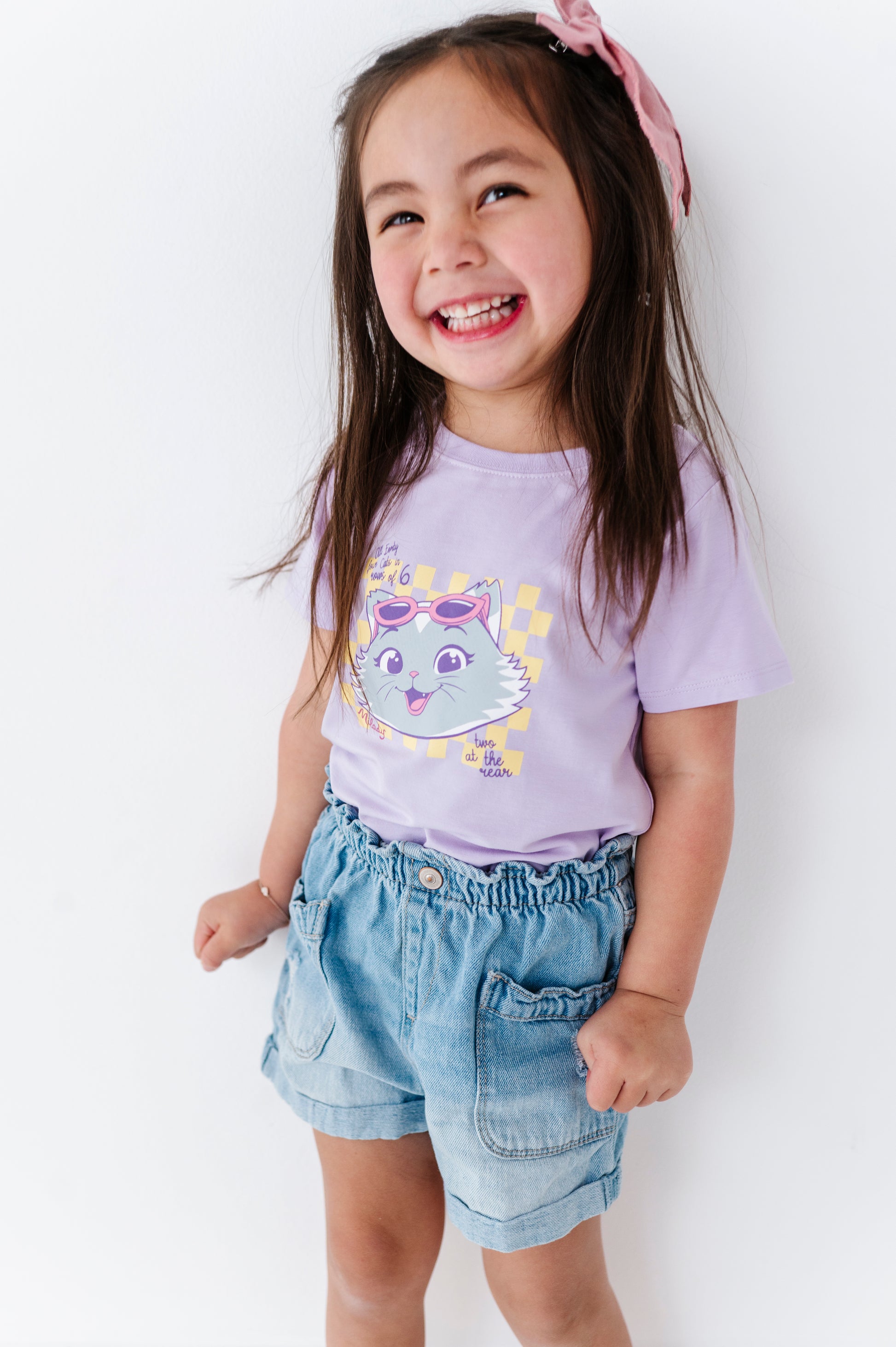 Young girl wearing a purple 44 Cats t-shirt and denim shorts on a white background
