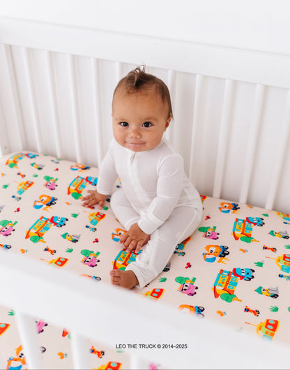 Baby sitting on a crib with colorful Leo the Truck bamboo fitted sheet 