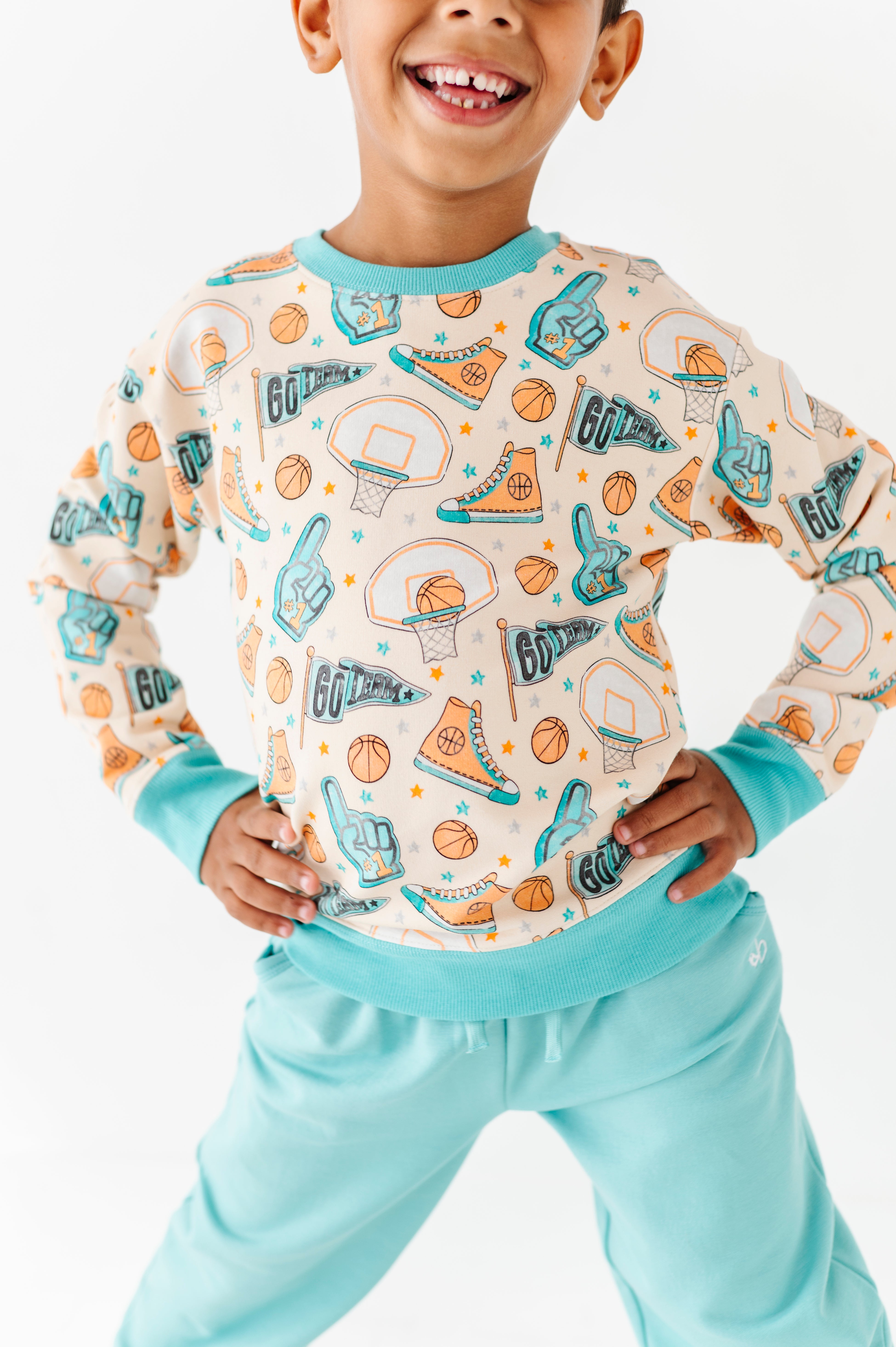 Child wearing a long-sleeve bamboo shirt with sports-themed design and light blue pants on a white background