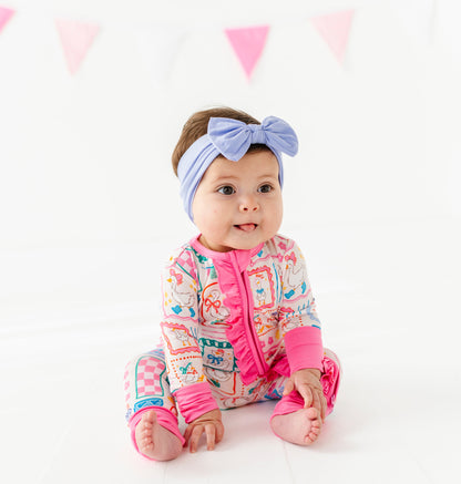 Baby wearing a colorful bamboo romper with pink accents and a headband, sitting on a white background with pink triangle flags.