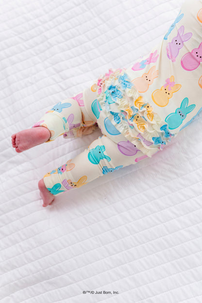 Baby legs wearing colorful romper with PEEPS® design on a white quilted surface.