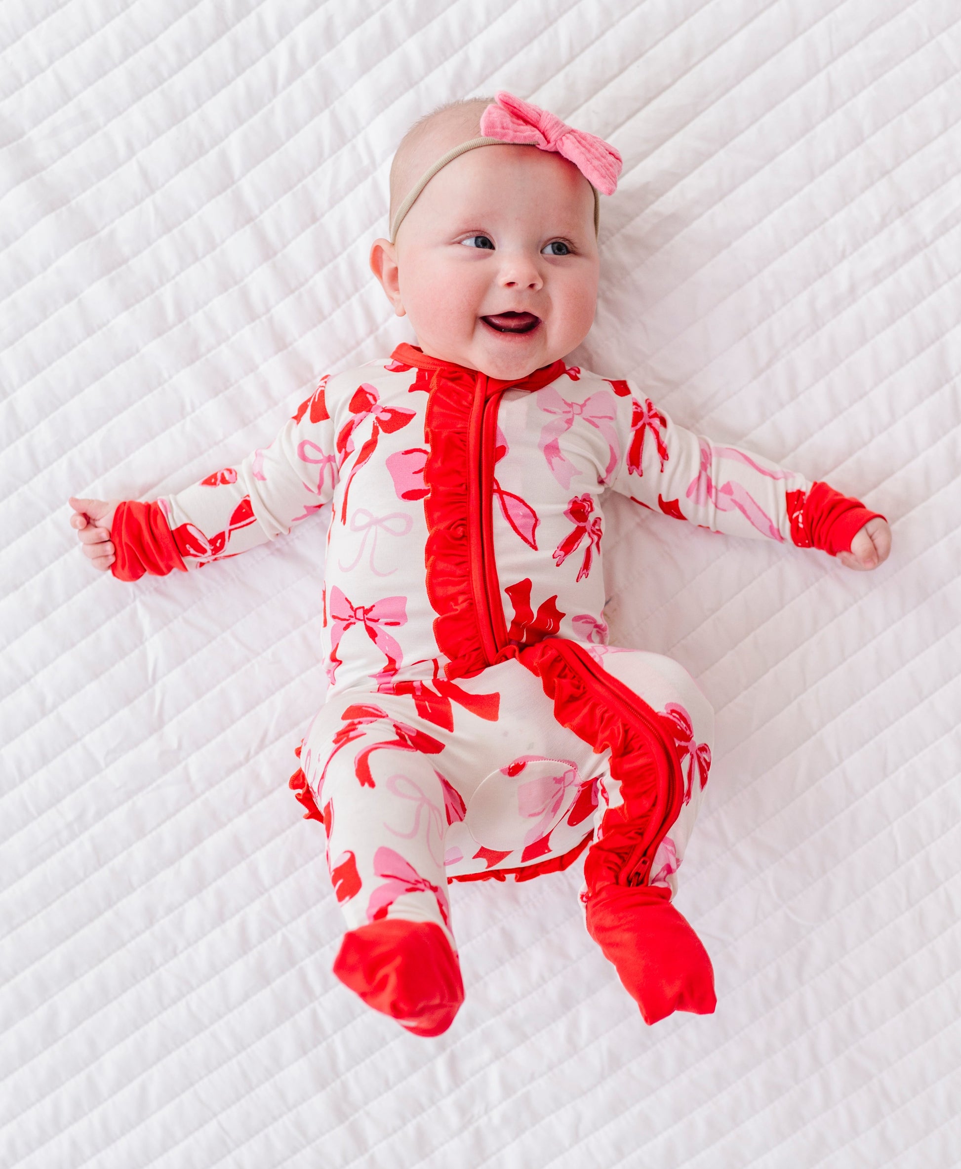 Baby lying down wearing pink bow print bamboo romper with fold-over feet cuffs