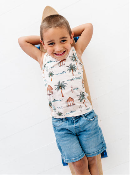 Child wearing a sleeveless shirt with palm tree design and denim shorts on a white background