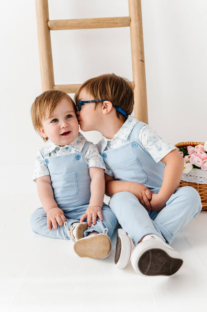 Two children in matching outfits sitting on a white floor with a wooden ladder in the background.