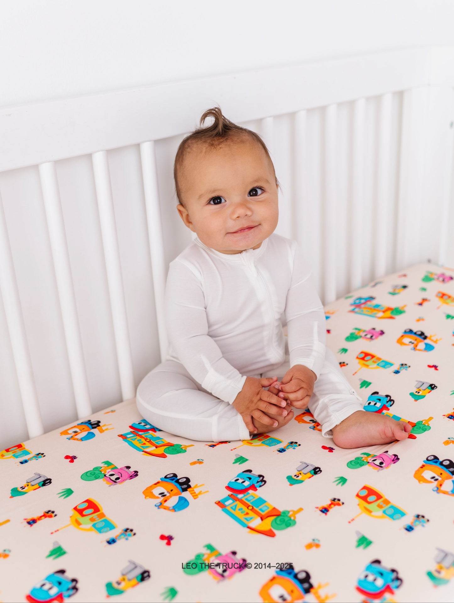 Baby sitting in a crib with Leo the Truck bamboo bedding