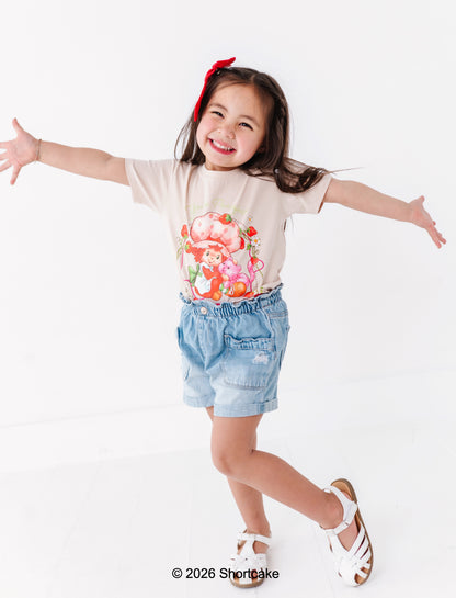 Child wearing a floral t-shirt and denim shorts with arms outstretched on a white background