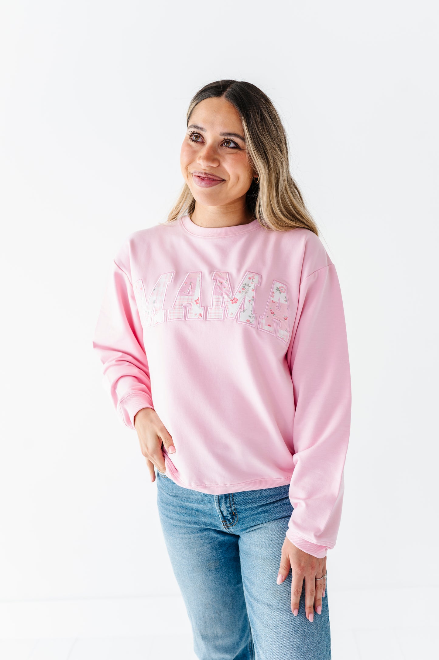 Woman wearing a pink bamboo-cotton sweatshirt with the word "MAMA" and blue jeans on a white background