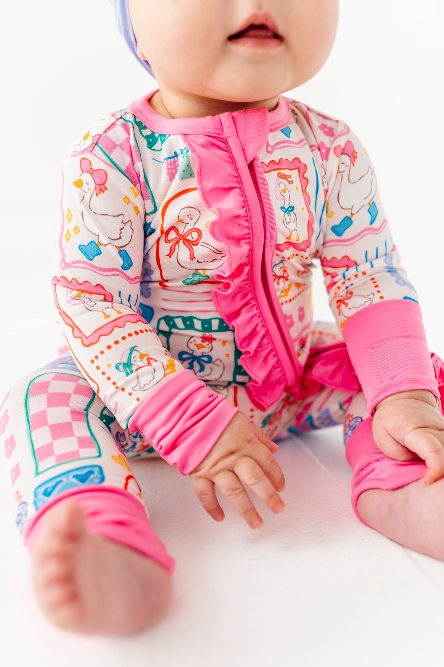 Baby in colorful bamboo geese romper with pink accents on a white background