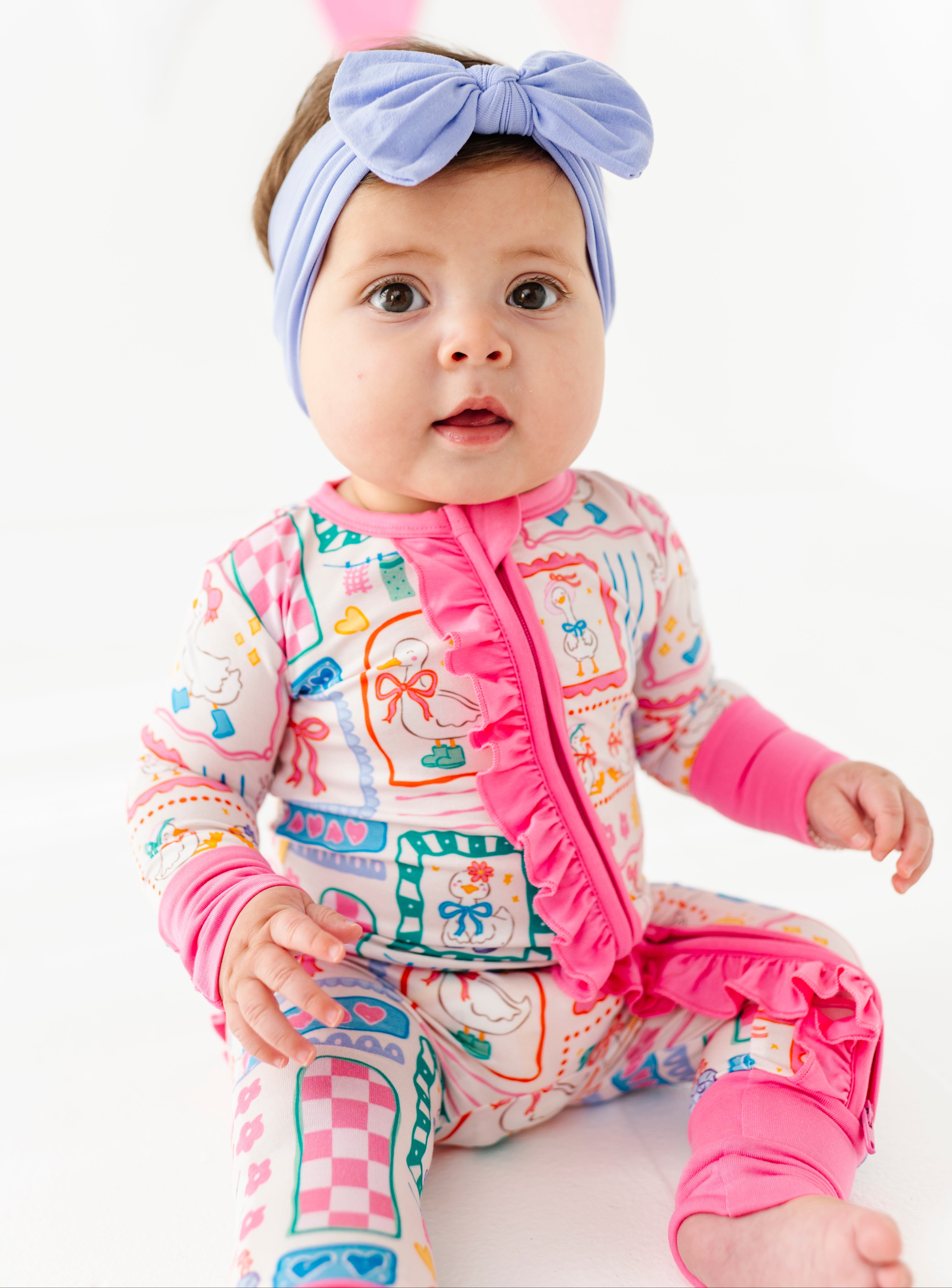 Baby wearing a colorful bamboo romper with pink ruffle and a headband on a white background