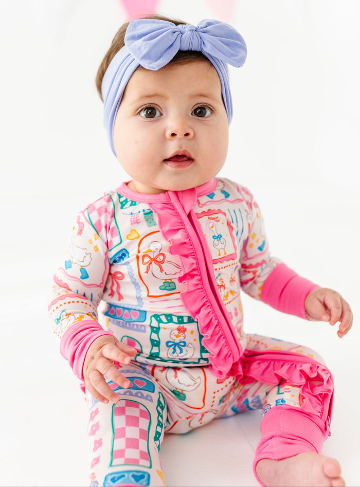 Baby wearing a colorful bamboo romper with pink ruffle and a headband on a white background