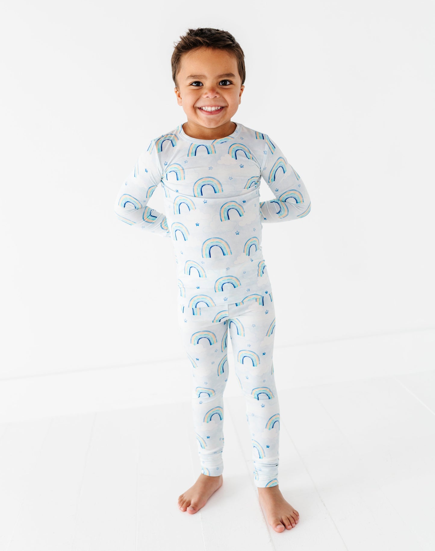 Child wearing a bamboo two-piece pajama set with blue rainbow patterns on a white background