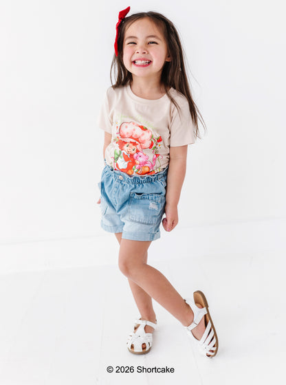 Young girl wearing a Strawberry Shortcake™ t-shirt and denim shorts on a white background